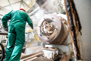 technician in protective gear servicing industrial pellet mill equipment for biomass wood pellets production in a sustainable energy factory