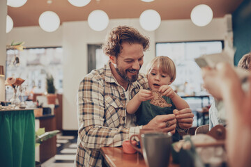 Loving father doing arts and crafts with his cute little son sitting on his lap during a family weekend activity together