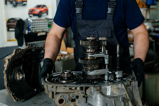 Repair of the manual gearbox of the car at the service station, focus on the disassembled mechanism, which the hands of the craftsman are engaged in