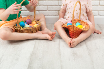 Unrecognizable children sitting on the floor with colorful Easter eggs in two wicker baskets
