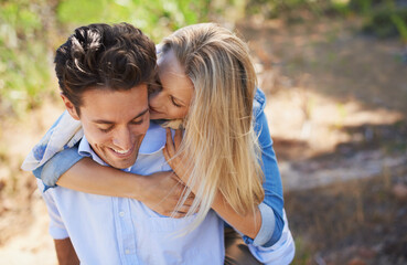 Happy couple, kiss and cheek in piggyback for love, bonding or support for outdoor affection in nature. Face of young woman and man smile for embrace, hug or romantic back ride in forest together