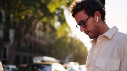 Pensive man in sunglasses and wireless earbuds listen audiobook while walk outdoors in slow motion. Confident male enjoy music from online playlist in earphones. Warm sunlight at summer evening
- Powered by Adobe