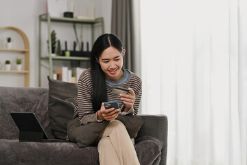 Happy young Asian woman doing online shopping on mobile phone with credit card