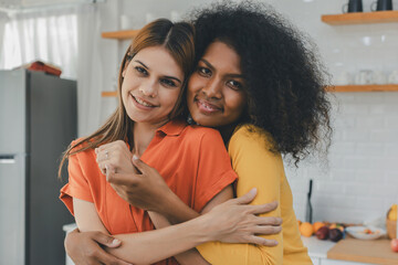 Multiethnic lesbian couple having embracing in kitchen room. black and white couple holding ring....