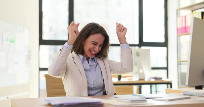 Adult business woman manager dances sitting at office desk and successful computer win