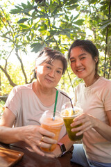 Happy asian Thai Chinese elder mother and daughter drinking together at cafe in garden, spending good time.