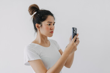 Asian Thai woman using mobile phone with funny doubt face, holding smartphone by silent suspicious, standing isolated over white background wall.