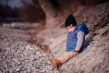 Curious toddler sitting on pebbles by the lake, exploring with a focused expression