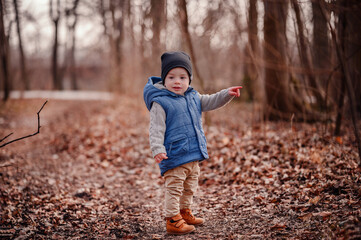 Young Explorer on Forest Path. A little boy in a vest pauses on a forest trail, a moment of...