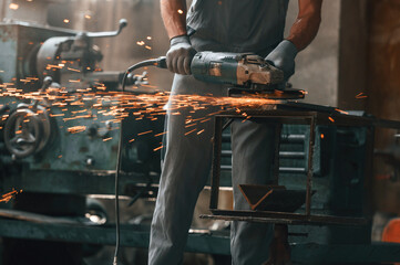 Polishing the surface with angle grinder. Close up view of man that is working at the factory