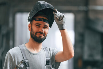 Welder man in safety helmet. Young factory worker in grey uniform