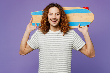 Young cheerful man he wears grey striped t-shirt casual clothes hold on shoulder skateboard pennyboard behind neck isolated on plain pastel light purple background studio portrait. Lifestyle concept.