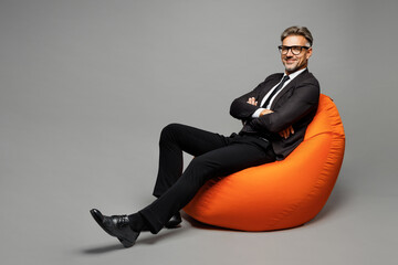 Full body adult employee business man corporate lawyer wear classic formal black suit shirt tie work in office sit in bag chair hold hands crossed folded look camera isolated on plain grey background.