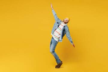 Fototapeta na wymiar Full body side view young man he wearing denim shirt hoody beanie hat casual clothes stand on toes with outstretched hands arms isolated on plain yellow background studio portrait. Lifestyle concept.