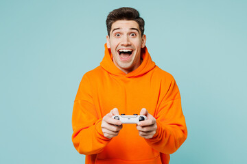 Young excited happy man wears orange hoody casual clothes hold in hand play pc game with joystick...