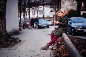 Urban Woman Texting on Street. Woman in winter attire using phone on city sidewalk