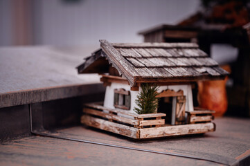 Miniature Wooden Cabin Model on Table. A detailed miniature wooden cabin with a shingled roof and a small pine tree