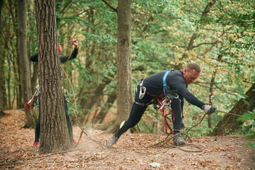 Naklejka premium Standing on the ground and preparing. Man is doing climbing in the forest by use of safety equipment