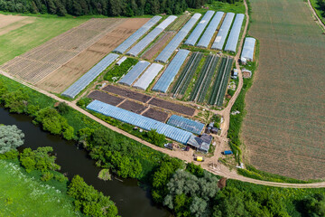 Aerial view of farmers' greenhouses in fields near the river