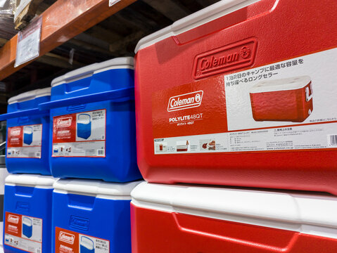 Rows of Coleman-brand red and blue coolers on display at a hypermart warehouse, indicating outdoor and storage themes.