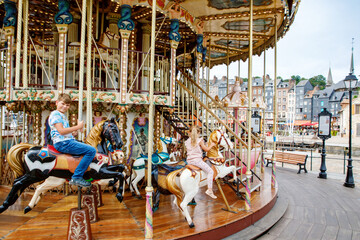 Adorable little girl and school kid boy having a ride on the old vintage merry-go-round in city of...