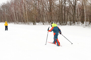 Boys in overalls goes skiing along the edge of the forest