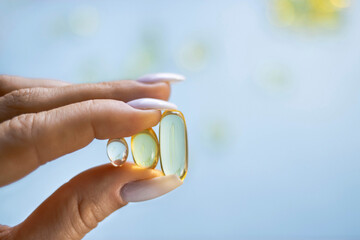 Young female hands are holding yellow omega 3 gel capsule close-up. Fish oil supplement. The...