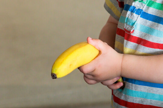 caucasian  Child hand holds a yellow unpeeled banana 