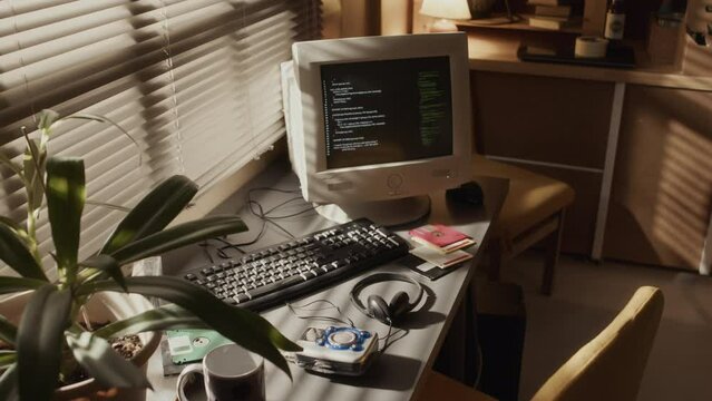 No people shot of old-fashioned desktop computer monitor with running program codes standing on desk in dimmed room with warm light from window blinds