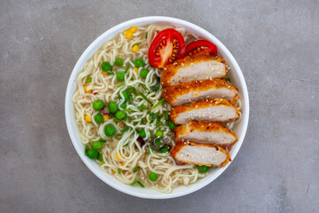 instant noodles or Ramen with crumbed chicken breast on mottled grey surface. Flat lay, top view with copy space
