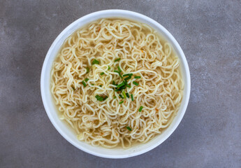 Plain instant noodles with chive garnish on mottled grey surface. Flat lay, top view with copy space