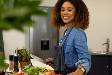 Portrait of happy biracial woman preparing food in kitchen chopping vegetables