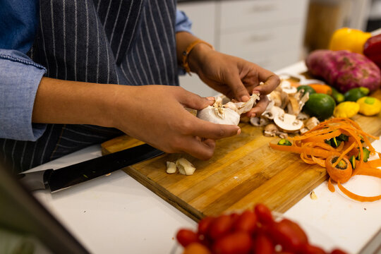 Midsection of biracial woman in apron preparing food in kitchen peeling garlic
