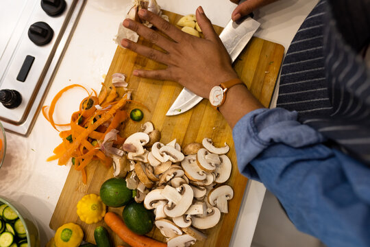 Midsection of biracial woman in apron preparing food in kitchen crushing garlic cloves