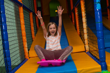 A little cheerful blonde girl slides down a slide in a children's entertainment center - 725397893