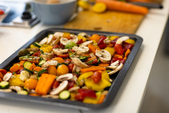 Seasoned chopped vegetables in baking tray on kitchen countertop