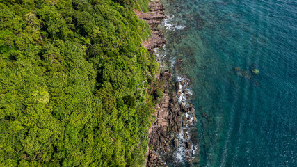 Aerial view of a lush green coastline merging with the clear blue waters of the ocean, highlighting...