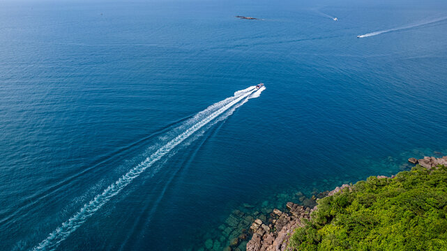 Aerial view of a speedboat cruising through blue sea waters near a tropical coast, creating a white wake trail, suitable for vacation and travel concepts
