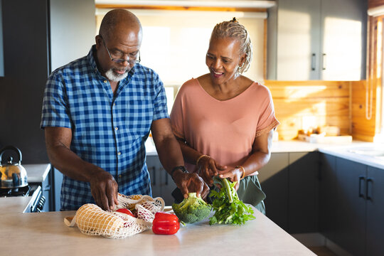 Happy senior african american couple unpacking groceries in kitchen