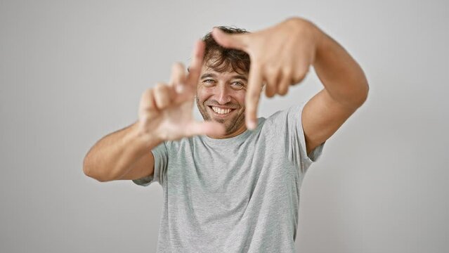 Beaming young man in casual t-shirt making a photo frame gesture with hands, filled with creativity and imagination. standout photography concept isolated on white background