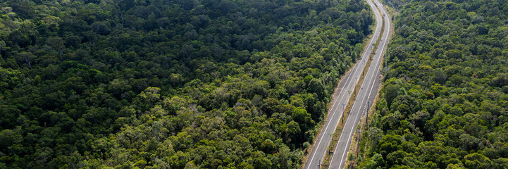 Fototapeta premium Aerial view of a highway cutting through a lush green forested landscape, symbolizing human infrastructure and transportation within natural environments