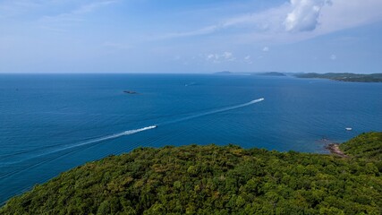 Aerial view of two speedboats leaving trails on a tranquil blue sea beside a lush green tropical coastline