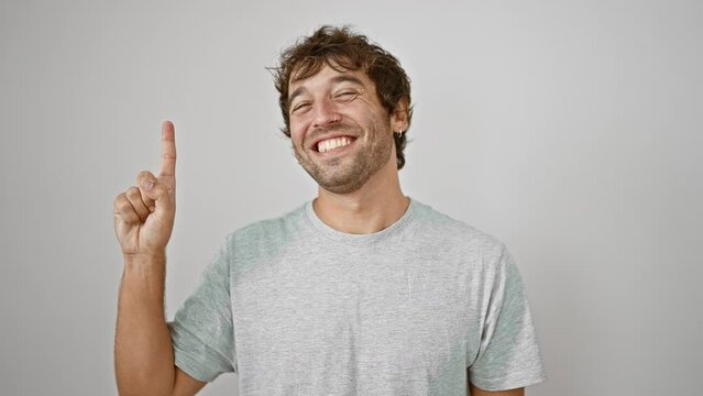 Cheerful young guy in a t-shirt, confidently raising his finger, pointing up. number one symbol, happily showing his positive expression against an isolated white background.
