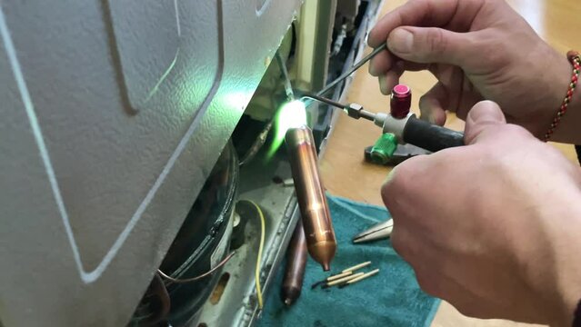 Fixing the refrigerator that not cooling enough by recharging Freon tube. Master attaches a tube with freon with a soldering iron