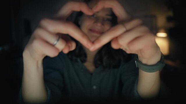 Close-up of hands of a young woman making a heart shape. Portrait of a Caucasian woman making a heart with her fingers while looking at the camera.