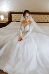 Fototapeta premium Portrait of the bride in the hotel room. A beautiful young girl is dressed in a white wedding dress. Modern wedding hairstyle. Natural makeup.