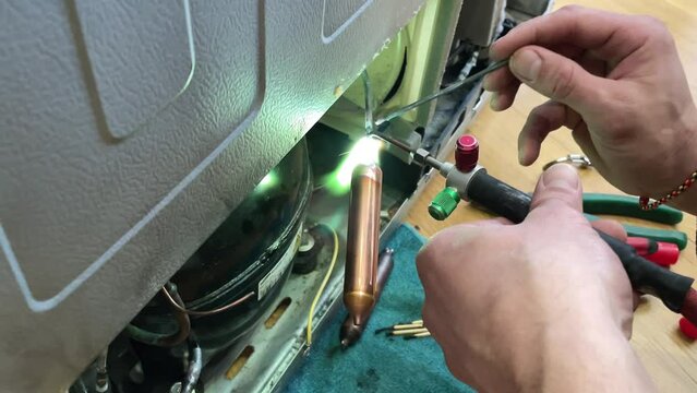Fixing the refrigerator that not cooling enough by recharging Freon tube. Master attaches a tube with freon with a soldering iron