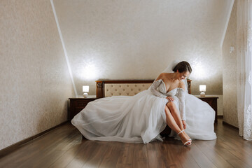 Young bride in beautiful wedding dress putting on shoes indoors. Bride dresses shoes before the...