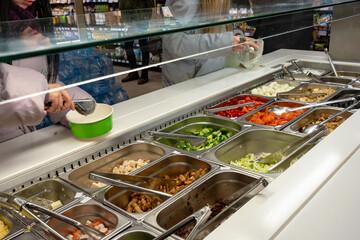 Fresh Salad bar counter with person's hands lifting vegetable into a salad bowl.