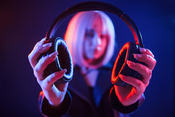 Showing headphones. Woman with white hair is in studio with neon colors